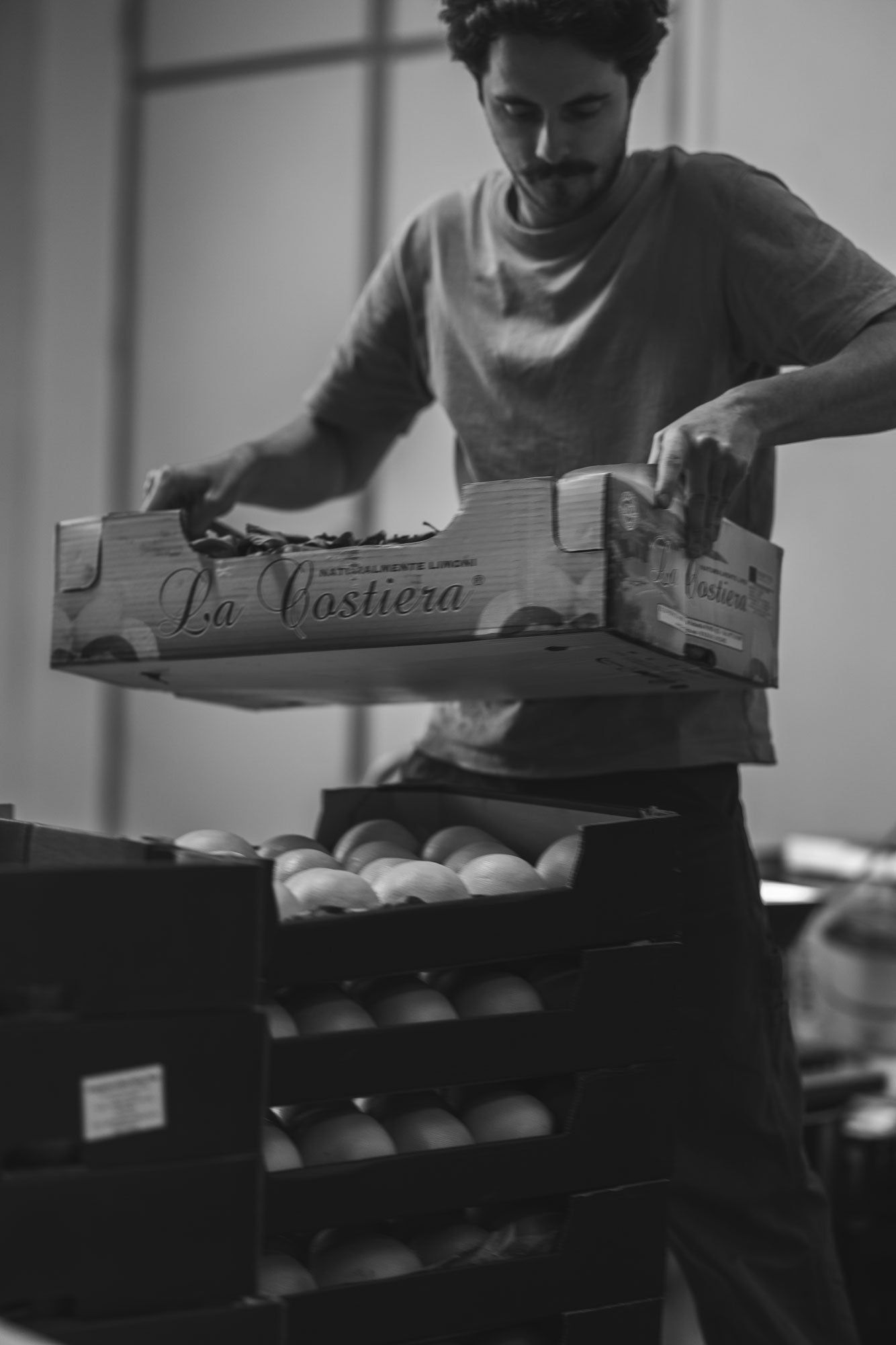 Person lifting a box labeled 'La Castiera' filled with Ceder lemons in a warehouse setting.